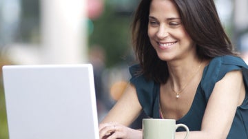 Una chica mira su portátil con una taza