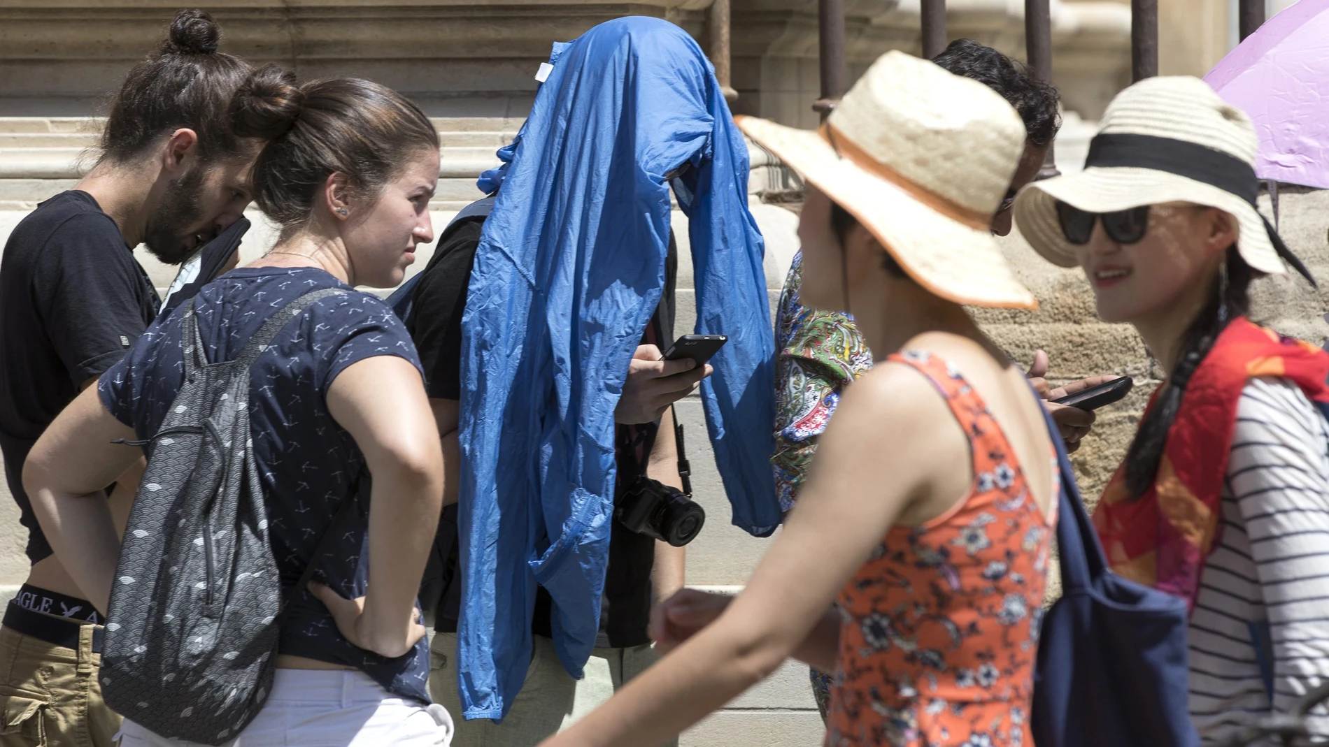 Un turista protegiéndose del sol con un chubasquero en la cabeza