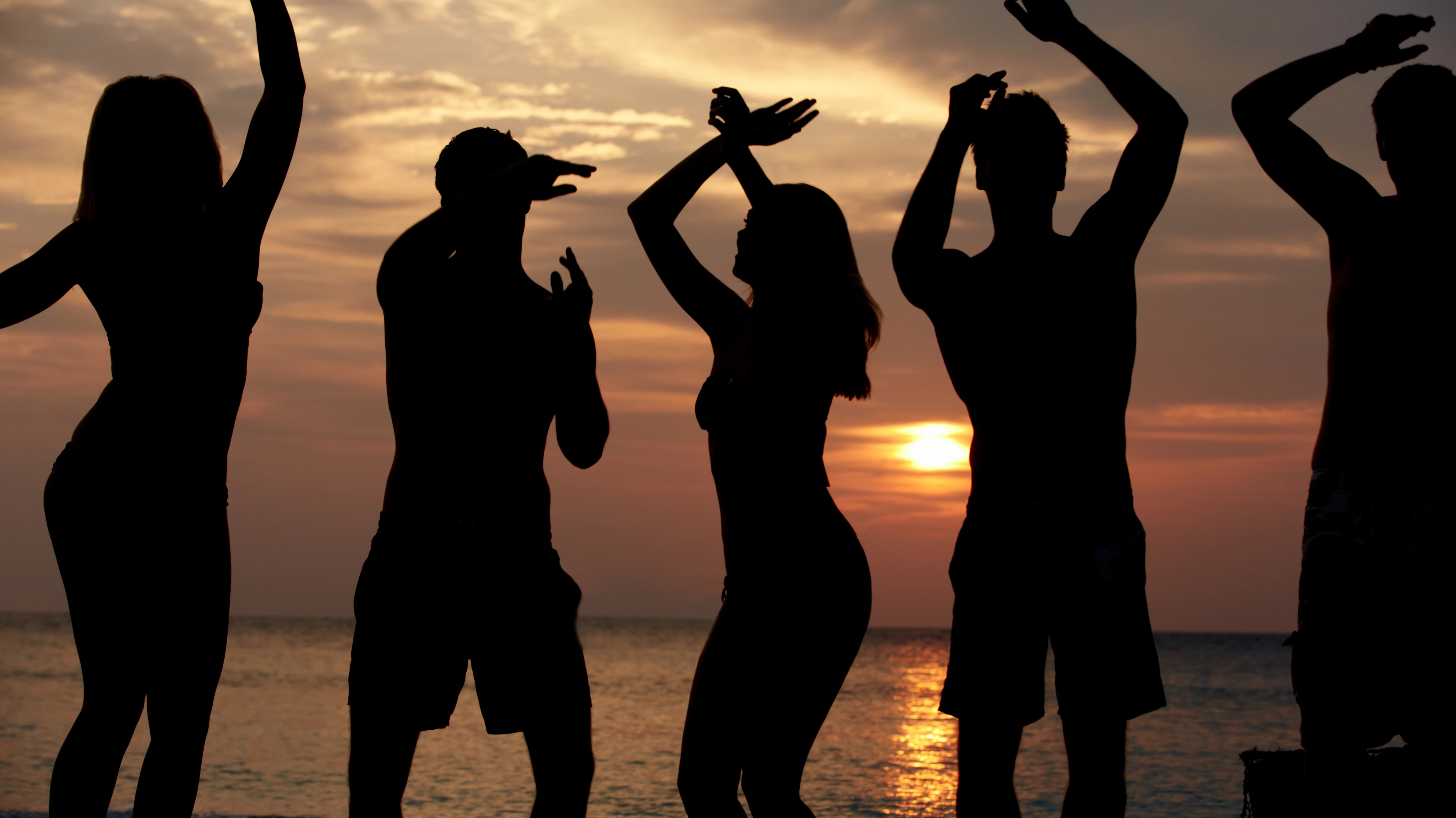 Siluetas de gente bailando en la playa