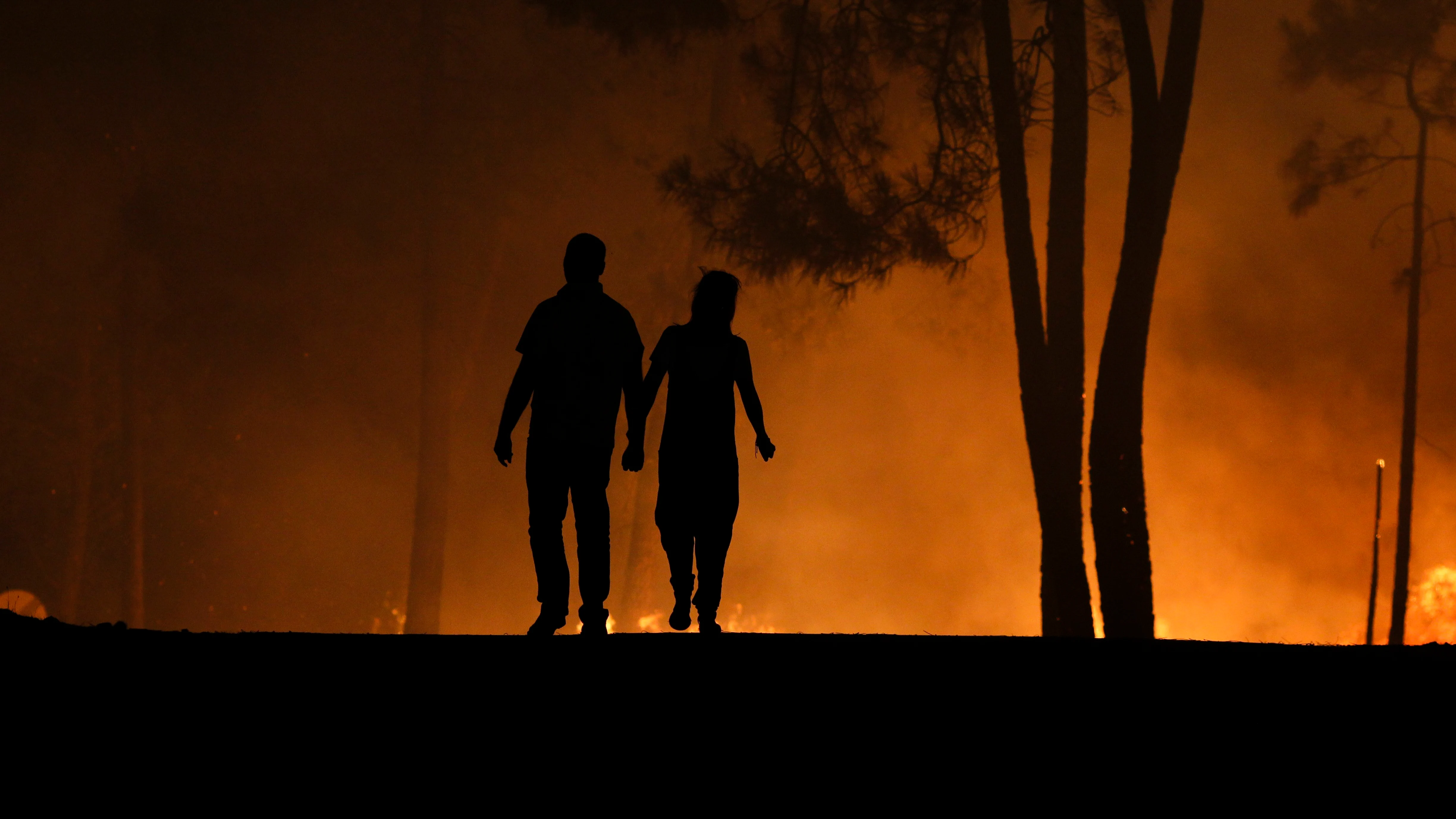 Un hombre y una mujer miran las llamas de un incendio forestal en Paredes, Vila de Rei, Centro de Portugal.