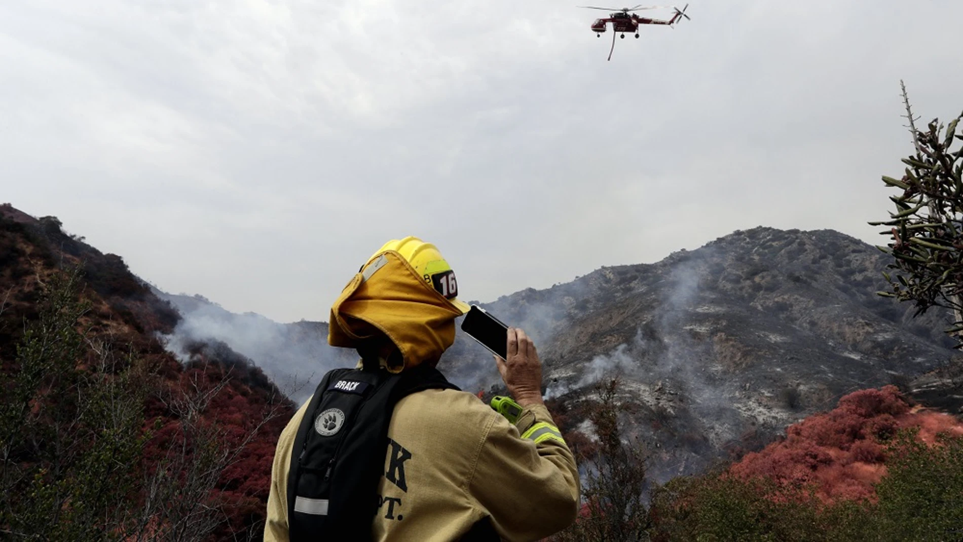 Un bombero y un helicóptero trabajan en las labores de extinción de el incendio de Los Ángeles