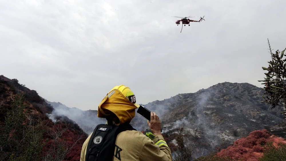 Un bombero y un helicóptero trabajan en las labores de extinción de el incendio de Los Ángeles