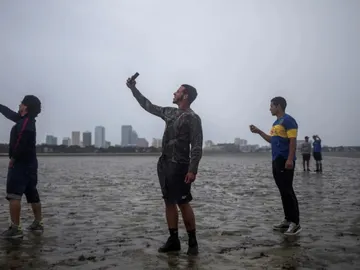 Varias personas se hacen selfies en la costa con el mar retirado Varias personas se hacen selfies en la costa con el mar retirado