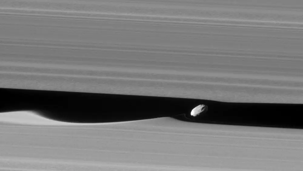 A medida que Daphnis, otra de las lunas de Saturno, orbita alrededor del planeta, su gravedad provoca olas en los anillos. Algunas partículas de estos quedan adheridas formando una especie de cresta sobre este satélite de tan solo 8 kilómetros de diámetro. 