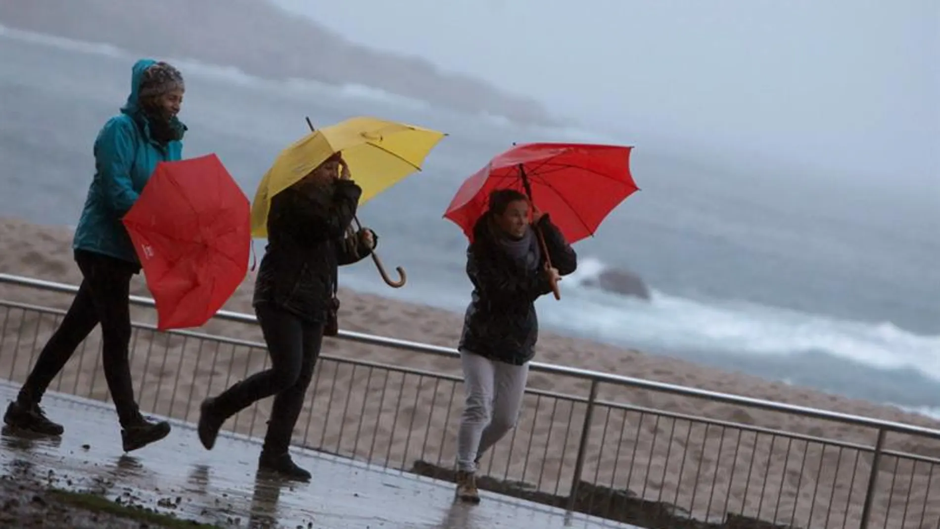 Tres mujeres se protegen de la lluvia en el paseo marítimo de A Coruña