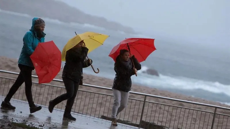 Tres mujeres se protegen de la lluvia en el paseo marítimo de A Coruña