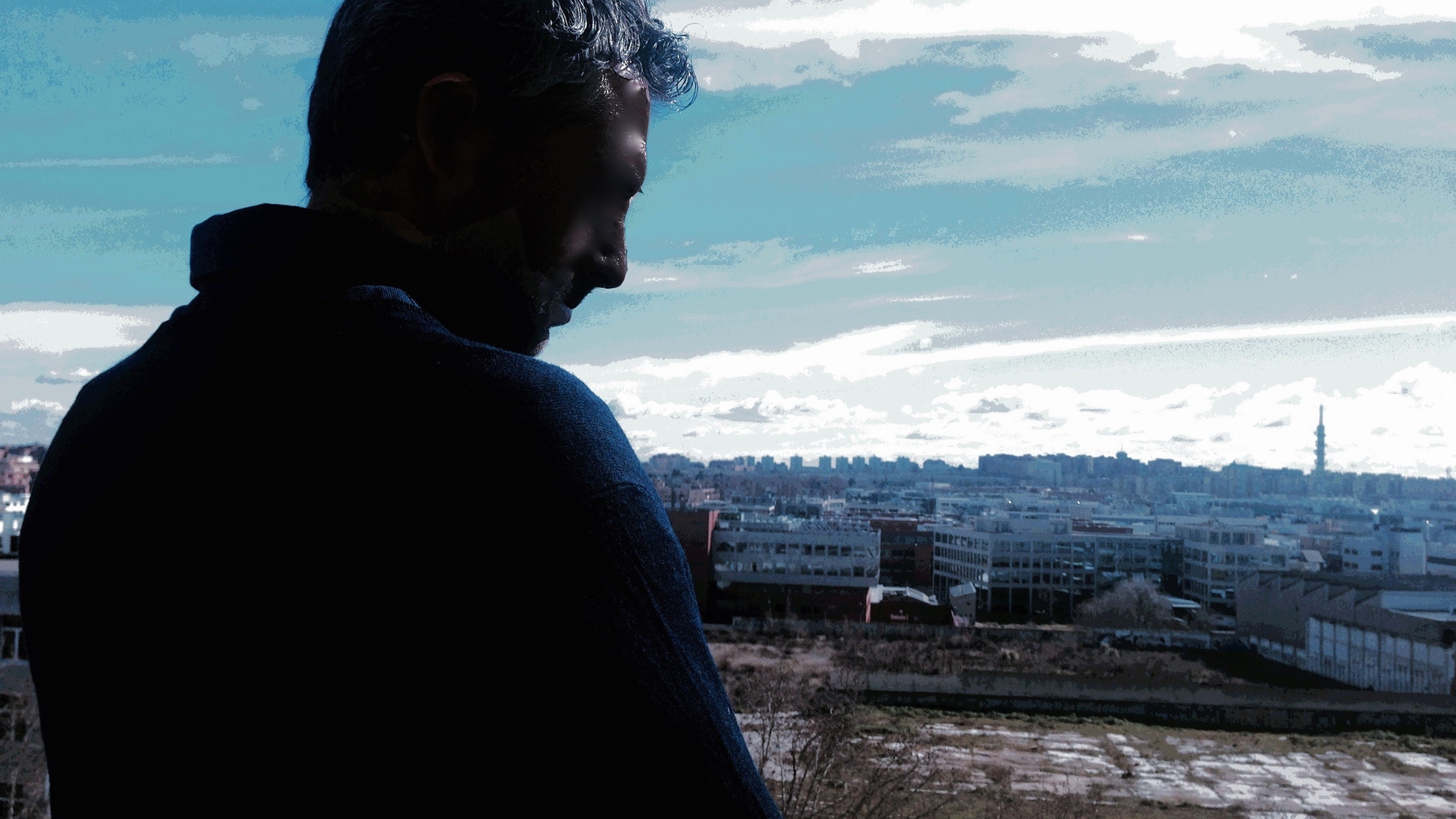 Fotomontaje titulado "La soledad". La autora es Laura Rico. Se ve de fondo un paisaje urbano frío y azulado. Y en primer término, de espaldas, la silueta a contraluz de un hombre que mira al suelo con aspecto triste. 