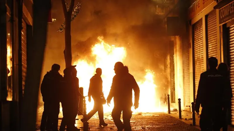 Contenedores incendiados en la calle Mesón de Paredes con la calle del Oso, en el barrio de Lavapiés