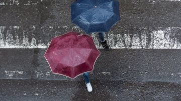 Dos personas cruzando un paso de cebra con paraguas