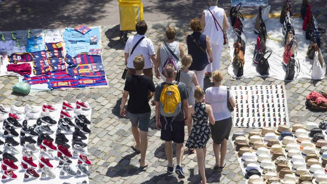 Unos turistas pasean por Las Ramblas de Barcelona entre varios manteros