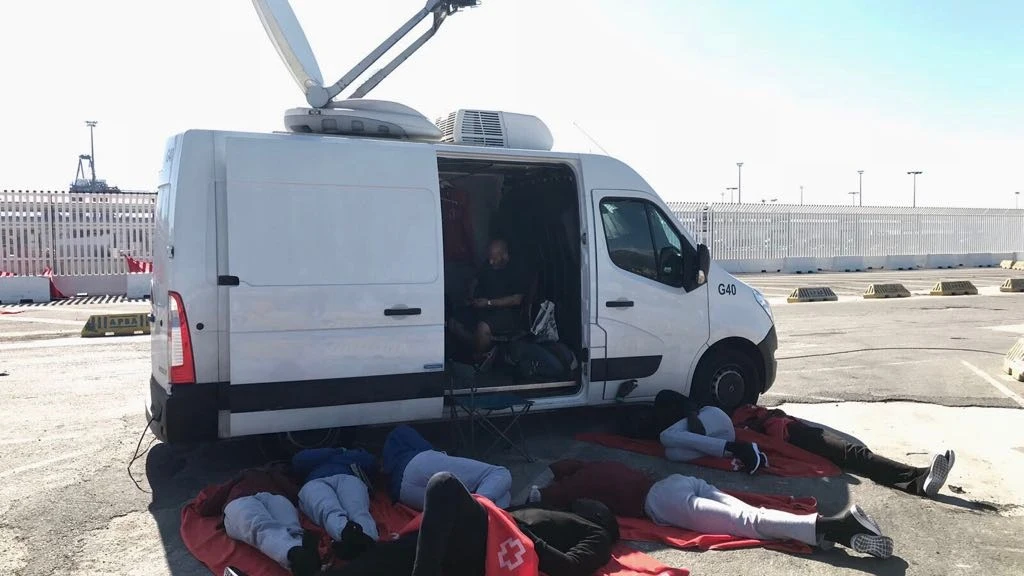 Un grupo de migrantes se resguardan del calor frente a una unidad móvil de laSexta.