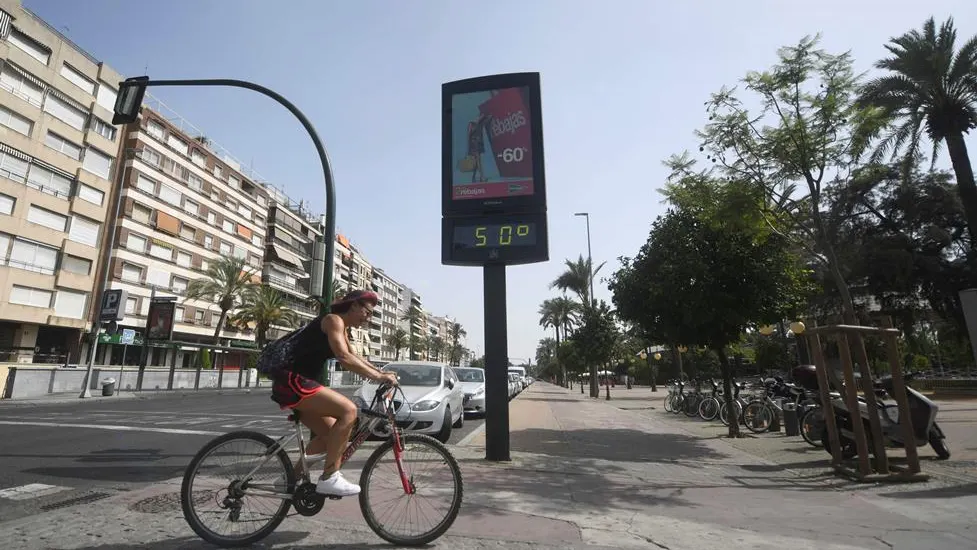 Un ciclista pasa junto a un termómetro que marca 50 grados en Córdoba, en una jornada marcada por la ola de calor que afecta a toda la Península