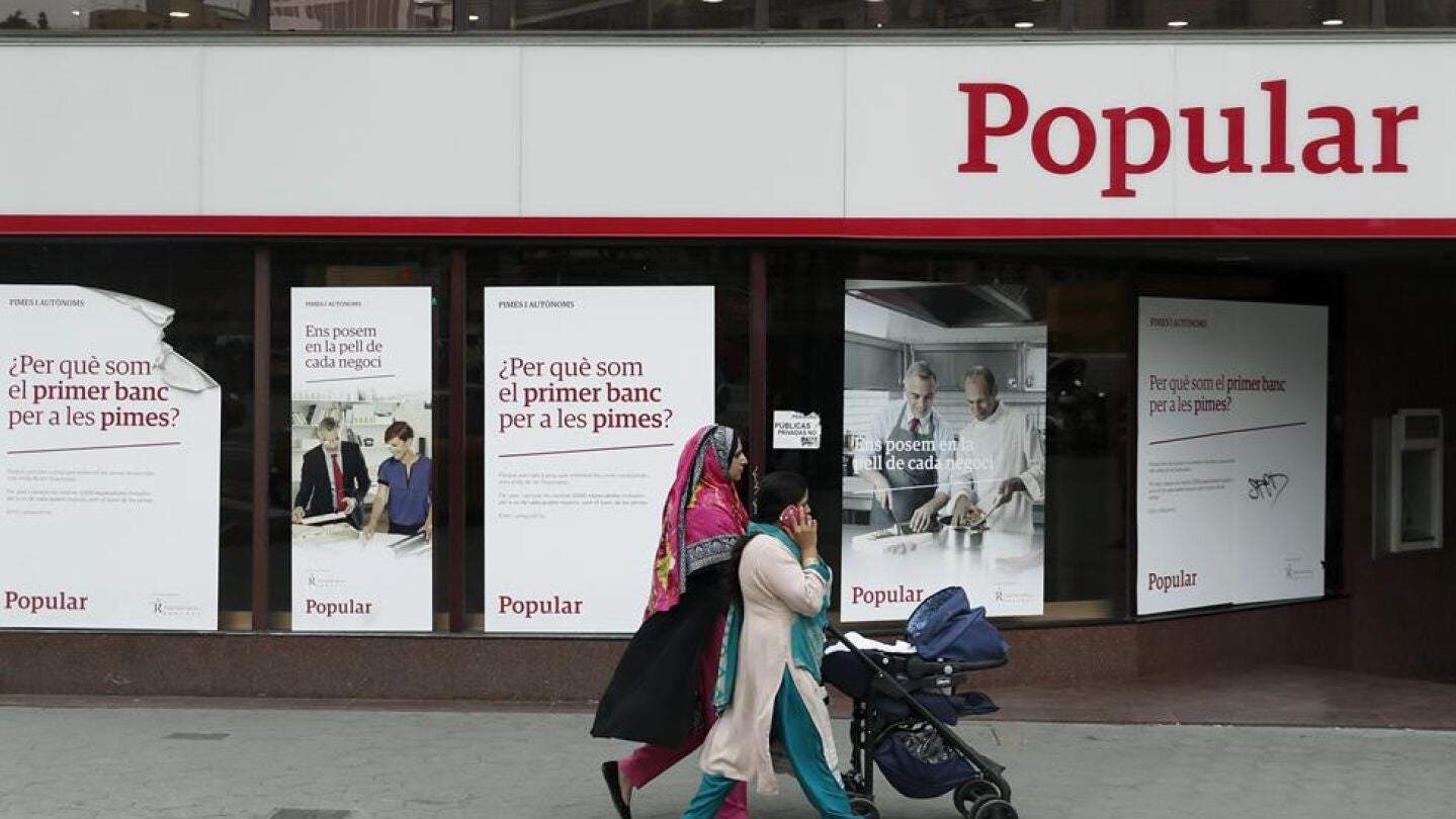 Unas mujeres pasan ante una oficina del Banco Popular. 