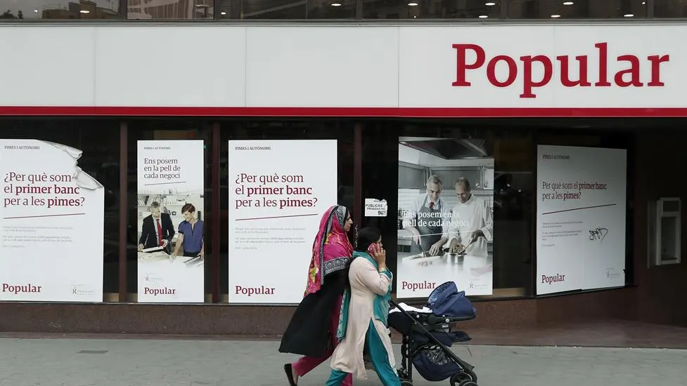 Unas mujeres pasan ante una oficina del Banco Popular. 