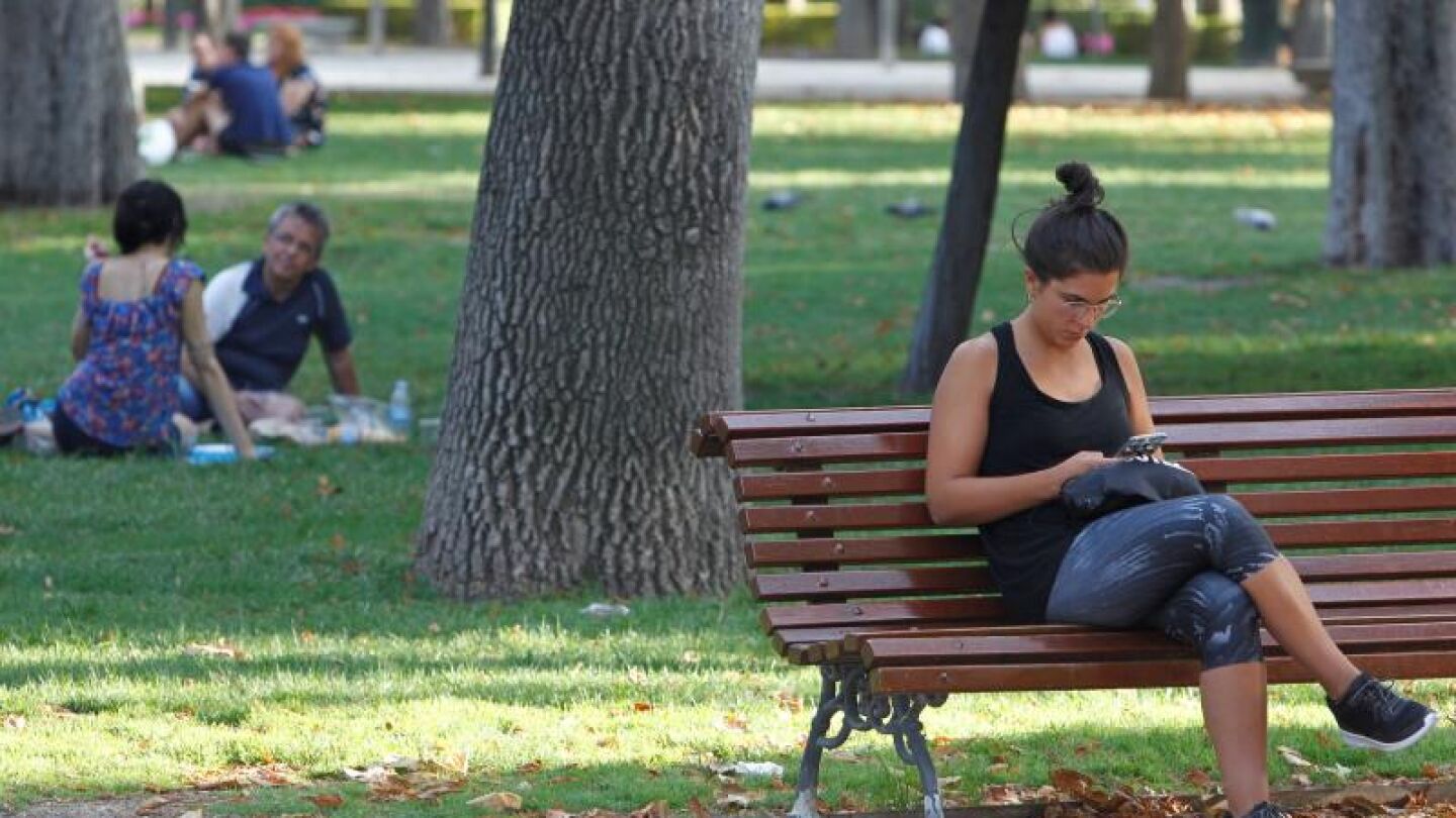 Imagen de archivo de una mujer que consulta su m&oacute;vil en un banco del madrile&ntilde;o parque del Retiro