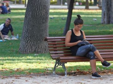 Imagen de archivo de una mujer que consulta su móvil en un banco del madrileño parque del Retiro Imagen de archivo de una mujer que consulta su móvil en un banco del madrileño parque del Retiro