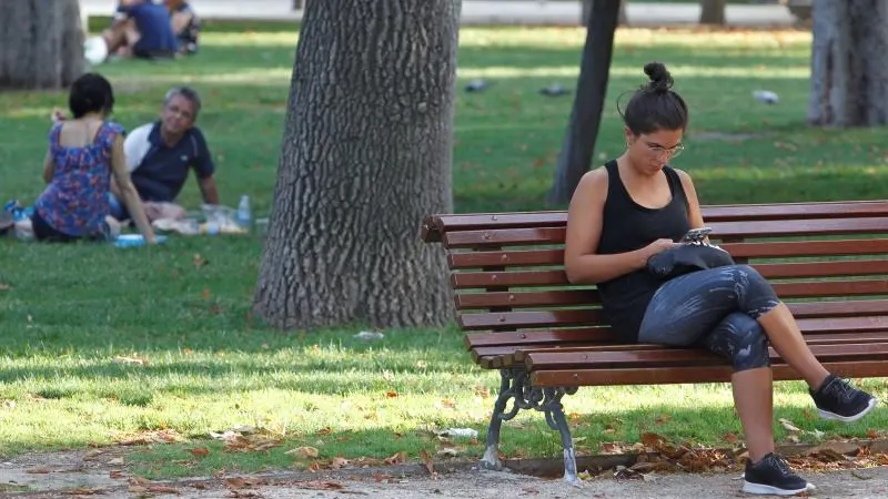 Imagen de archivo de una mujer que consulta su móvil en un banco del madrileño parque del Retiro