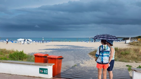 Dos mujeres se resguardan de la lluvia bajo un paraguas en una playa de Menorca Dos mujeres se resguardan de la lluvia bajo un paraguas en una playa de Menorca