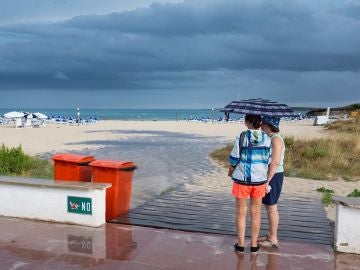 Dos mujeres se resguardan de la lluvia bajo un paraguas en una playa de Menorca Dos mujeres se resguardan de la lluvia bajo un paraguas en una playa de Menorca