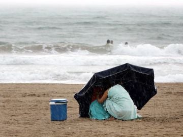 Una mujer se protege de la lluvia con su sombrilla en la playa de la Malvarrosa bajo la lluvia Una mujer se protege de la lluvia con su sombrilla en la playa de la Malvarrosa bajo la lluvia