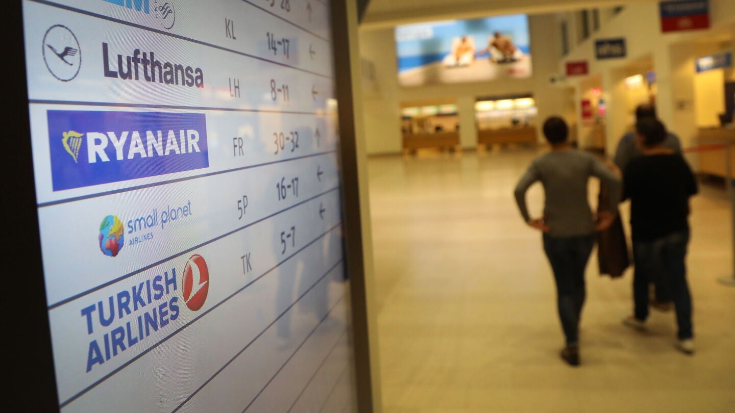Pasajeros caminan frente a una pantalla con el logo de la aerol&iacute;nea de bajo coste irlandesa Ryanair 