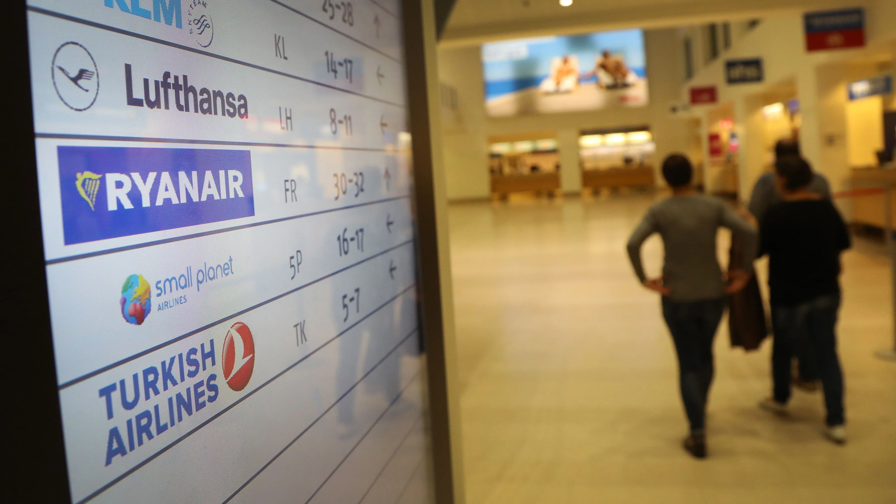 Pasajeros caminan frente a una pantalla con el logo de la aerolínea de bajo coste irlandesa Ryanair 