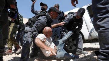 Soldados israelíes detienen a un palestino mientras los manifestantes bloquean el paso a una excavadora del ejército israelí 