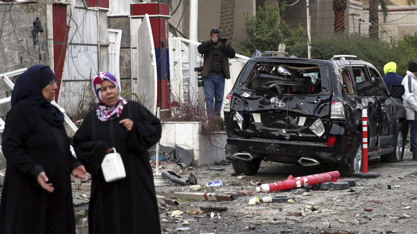Un grupo de personas permanece en el lugar donde explot&oacute; un coche bomba, en Bagdad, Irak