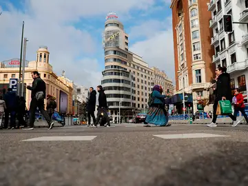 Viandantes cruzan la Gran vía de Madrid a la altura de la plaza de Callao
