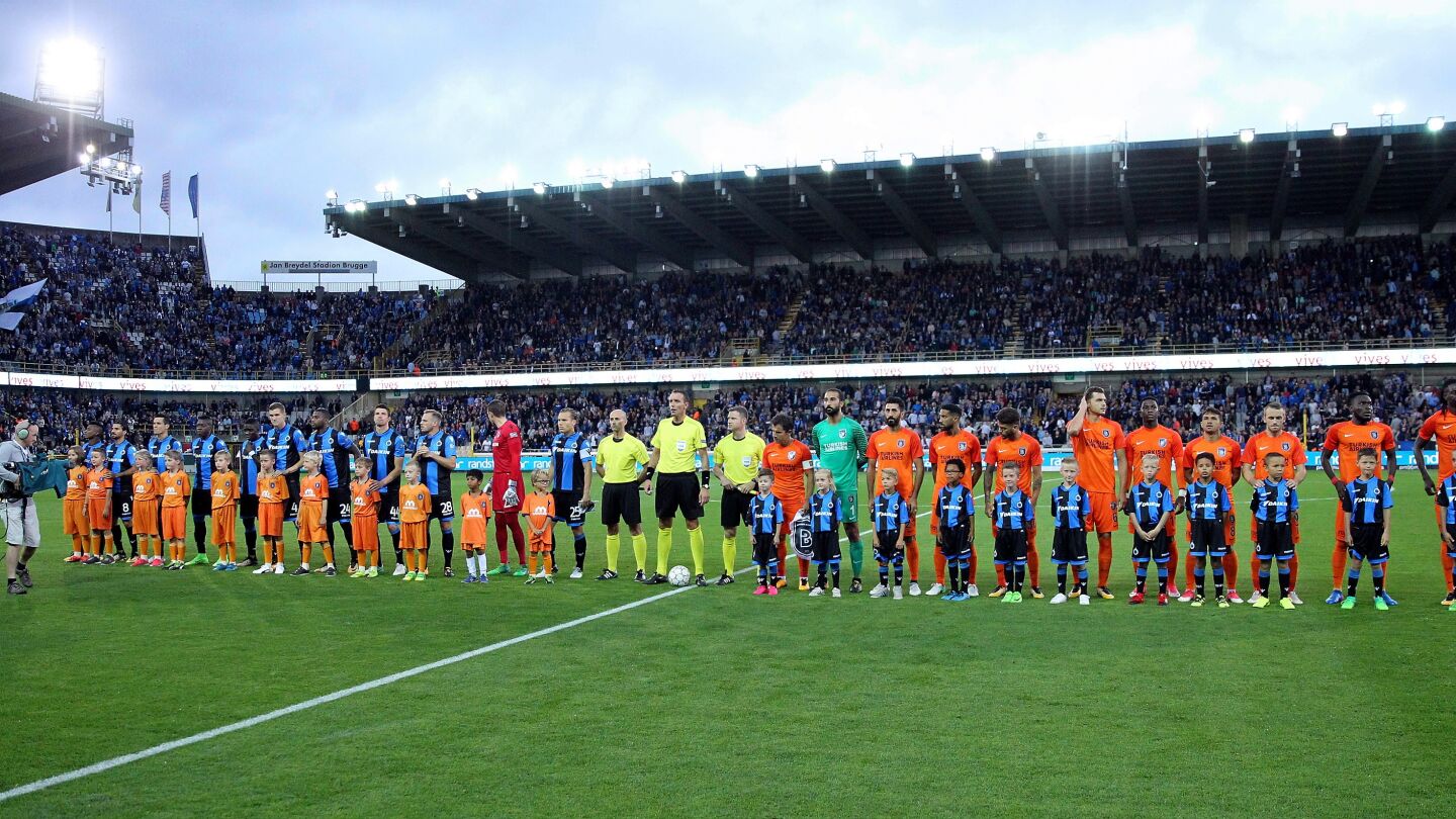 Los jugadores del Brujas (izquierda) escuchan el himno antes de un partido