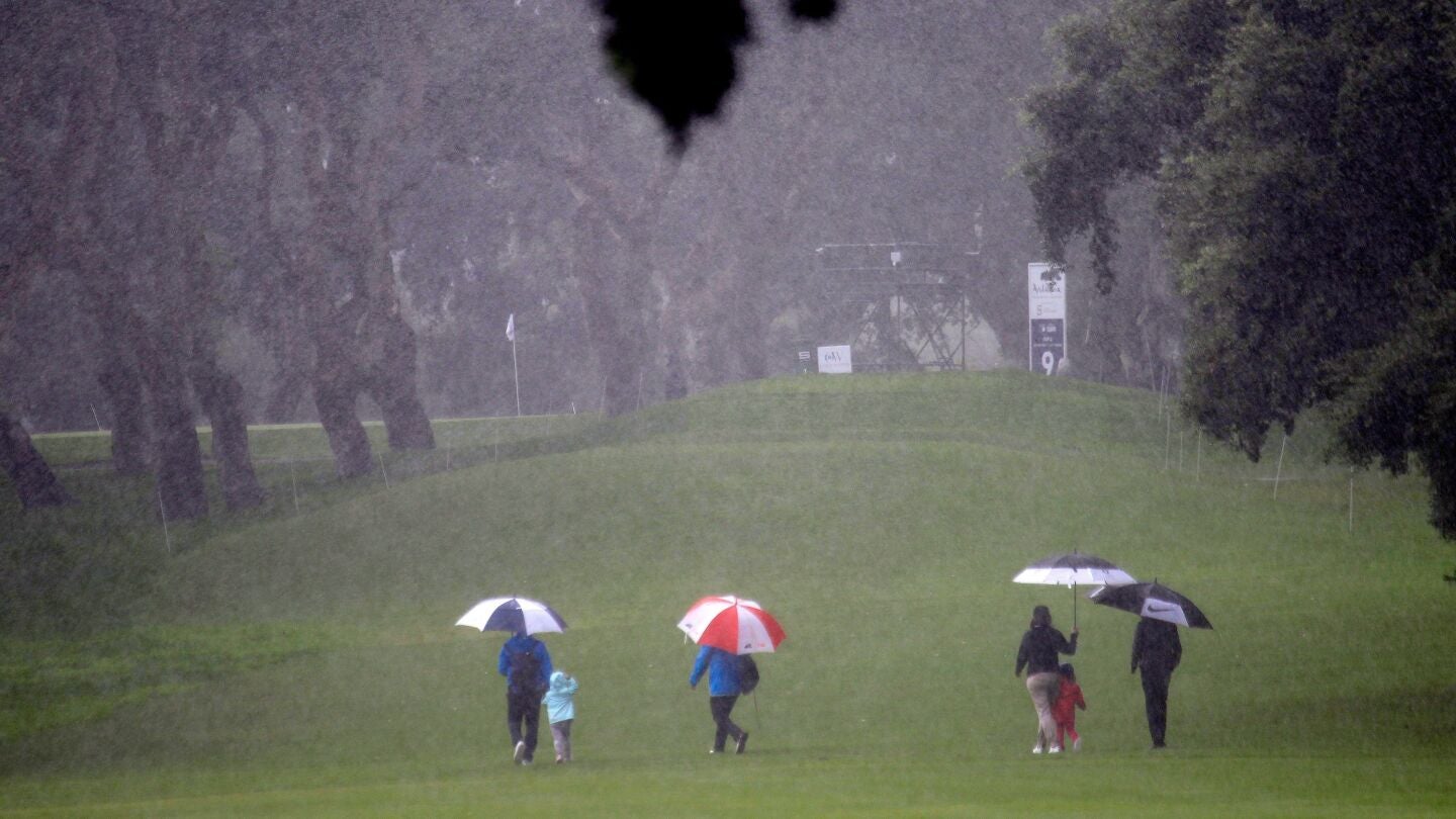 Espectadores cruzan bajo la fuerte lluvia uno de los hoyos del campo del Real Club