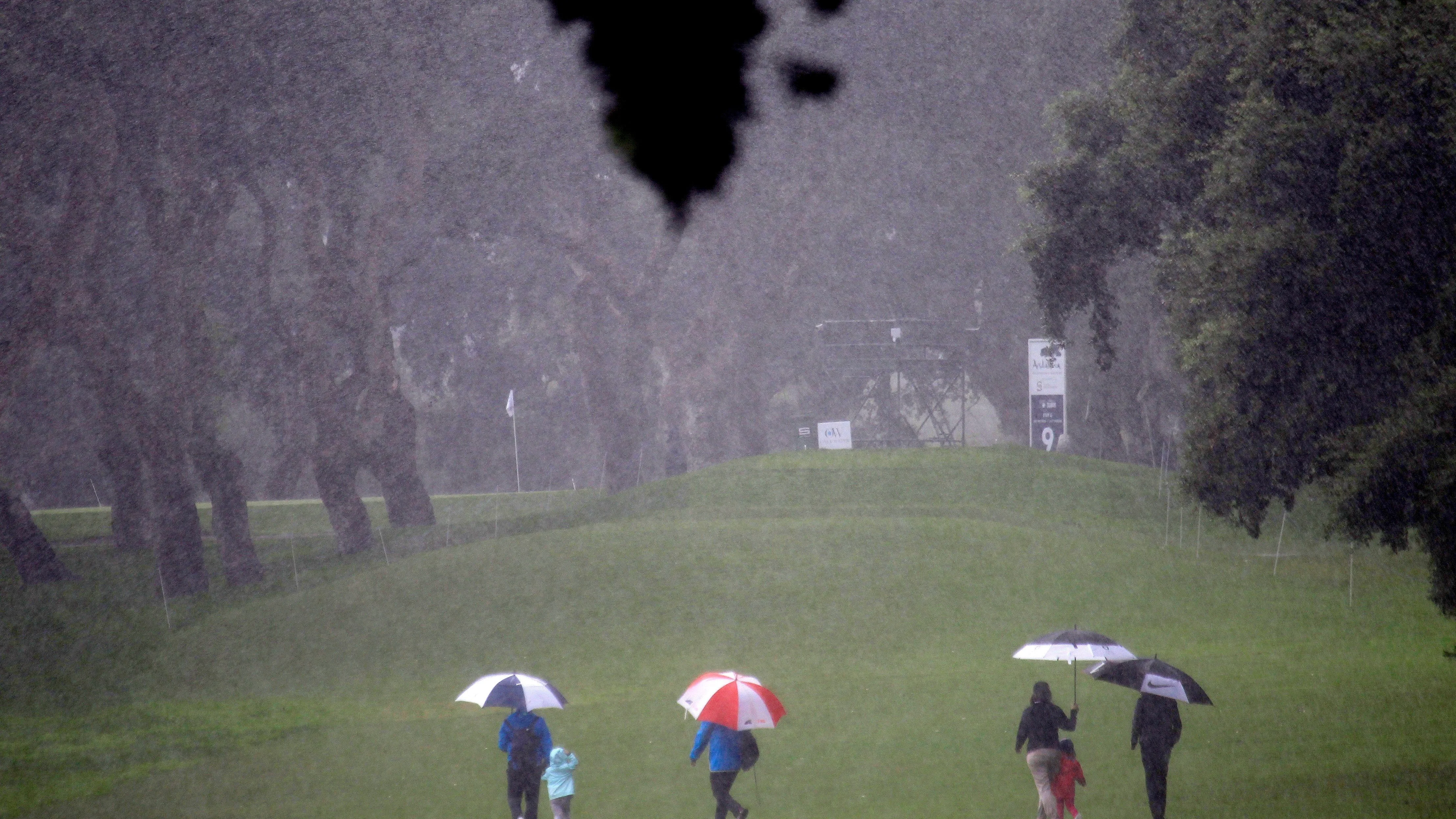 Espectadores cruzan bajo la fuerte lluvia uno de los hoyos del campo del Real Club