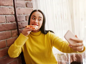 Chica grabándose en Instagram Stories mientras come una pizza Chica grabándose en Instagram Stories mientras come una pizza