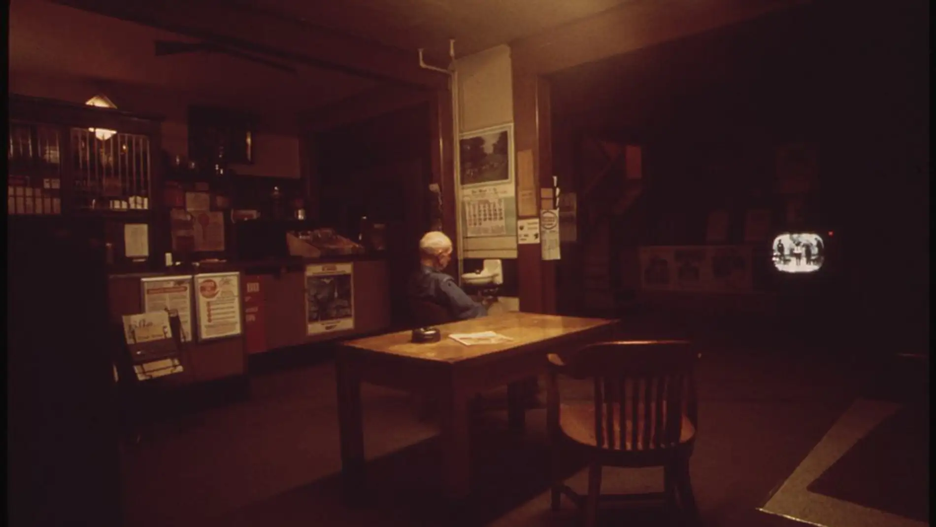 Fotografía en penumbra de una persona mayor viendo la televisión en un bar.