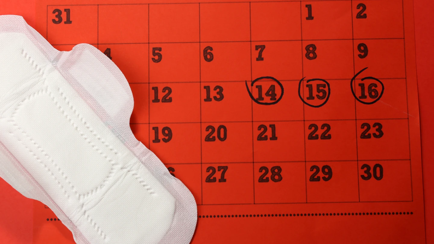 Un calendario menstrual junto a una compresa Un calendario menstrual junto a una compresa