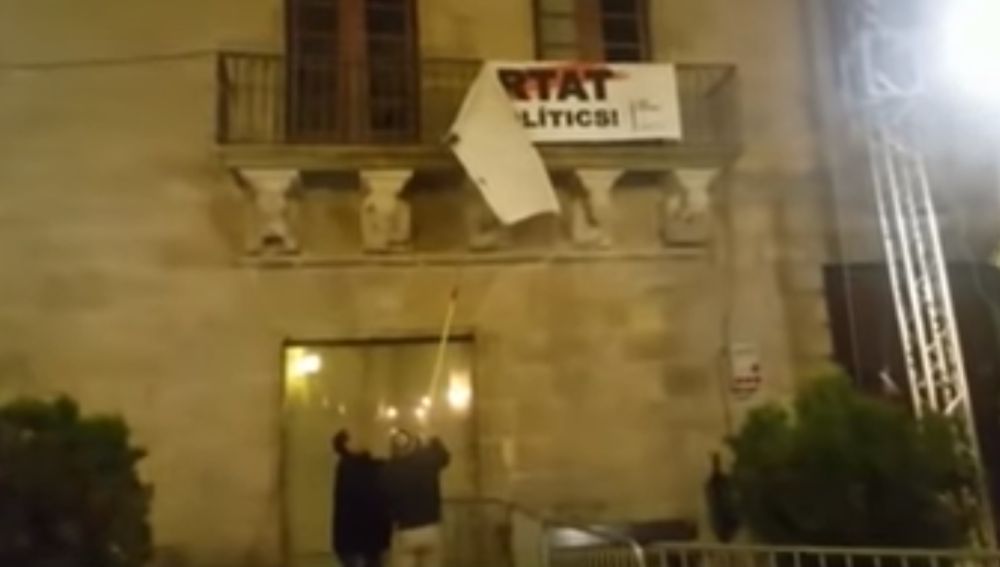 Dos personas descuelgan la pancarta por los políticos presos del balcón del Ayuntamiento de Cervera