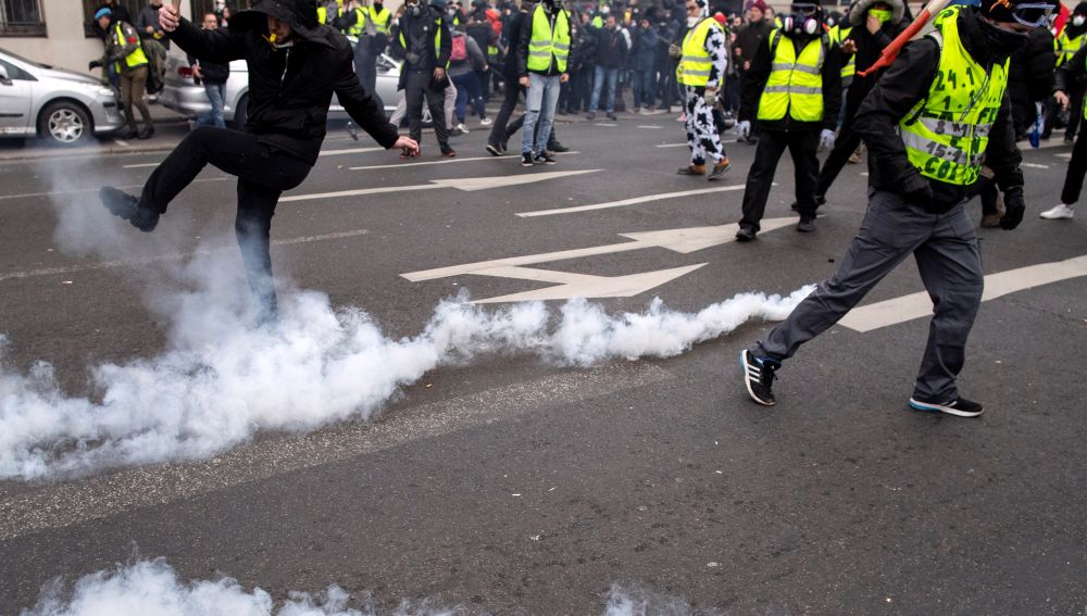 Varios "chalecos amarillos equivan botes de humo lanzados durante la protesta que hoy ha vuelto a recorrer las calles de París