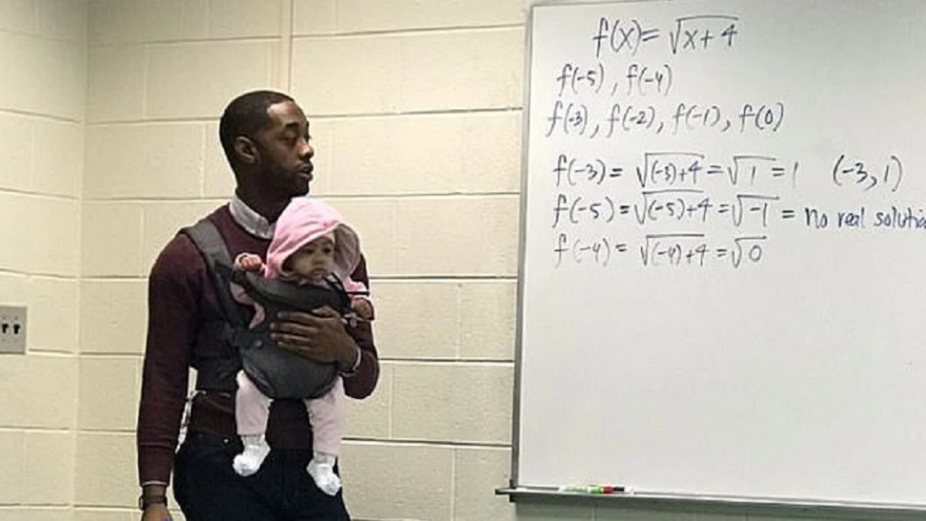 Imagen de un profesor con una bebé en brazos mientras daba clase