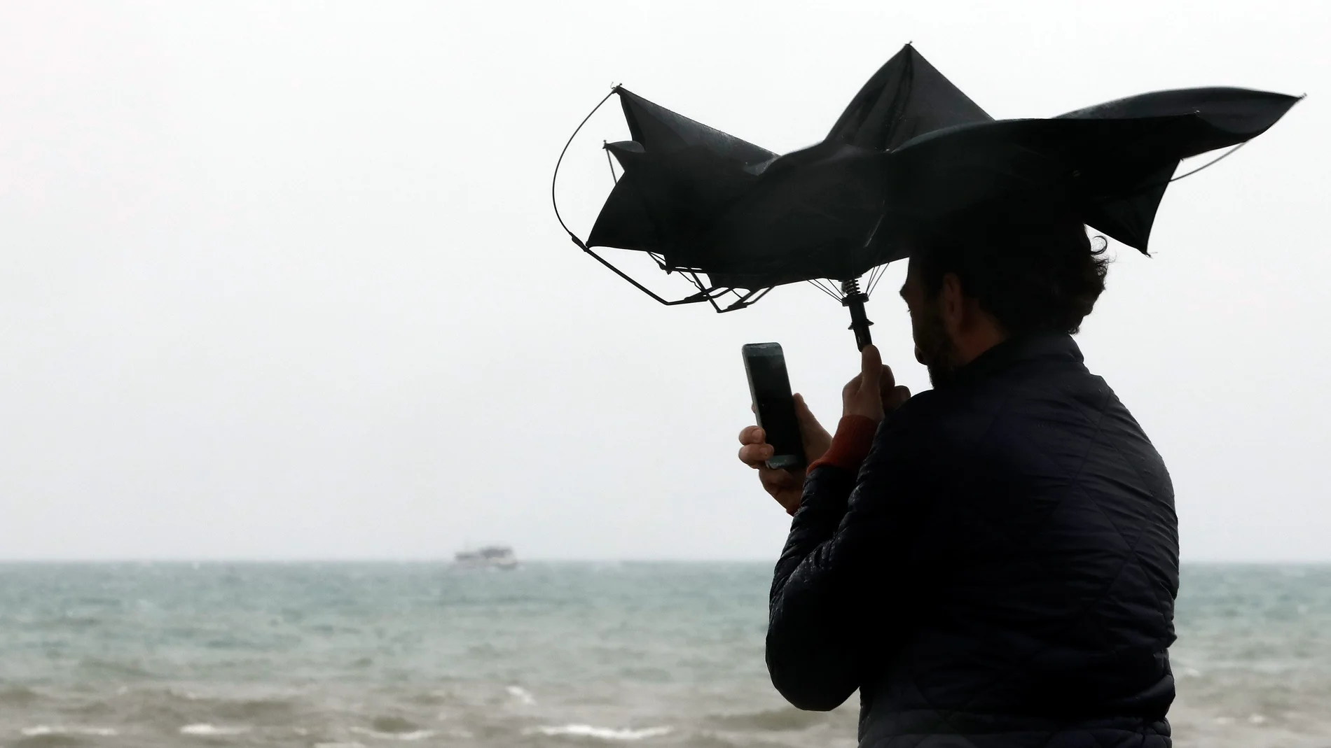 Imagen de archivo de una persona en la Playa de la Malvarrosa de Valéncia bajo la lluvia y el fuerte viento.