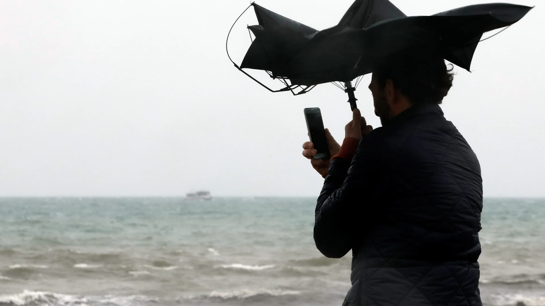 Una persona en la Playa de la Malvarrosa de Valéncia bajo la lluvia y el fuerte viento.