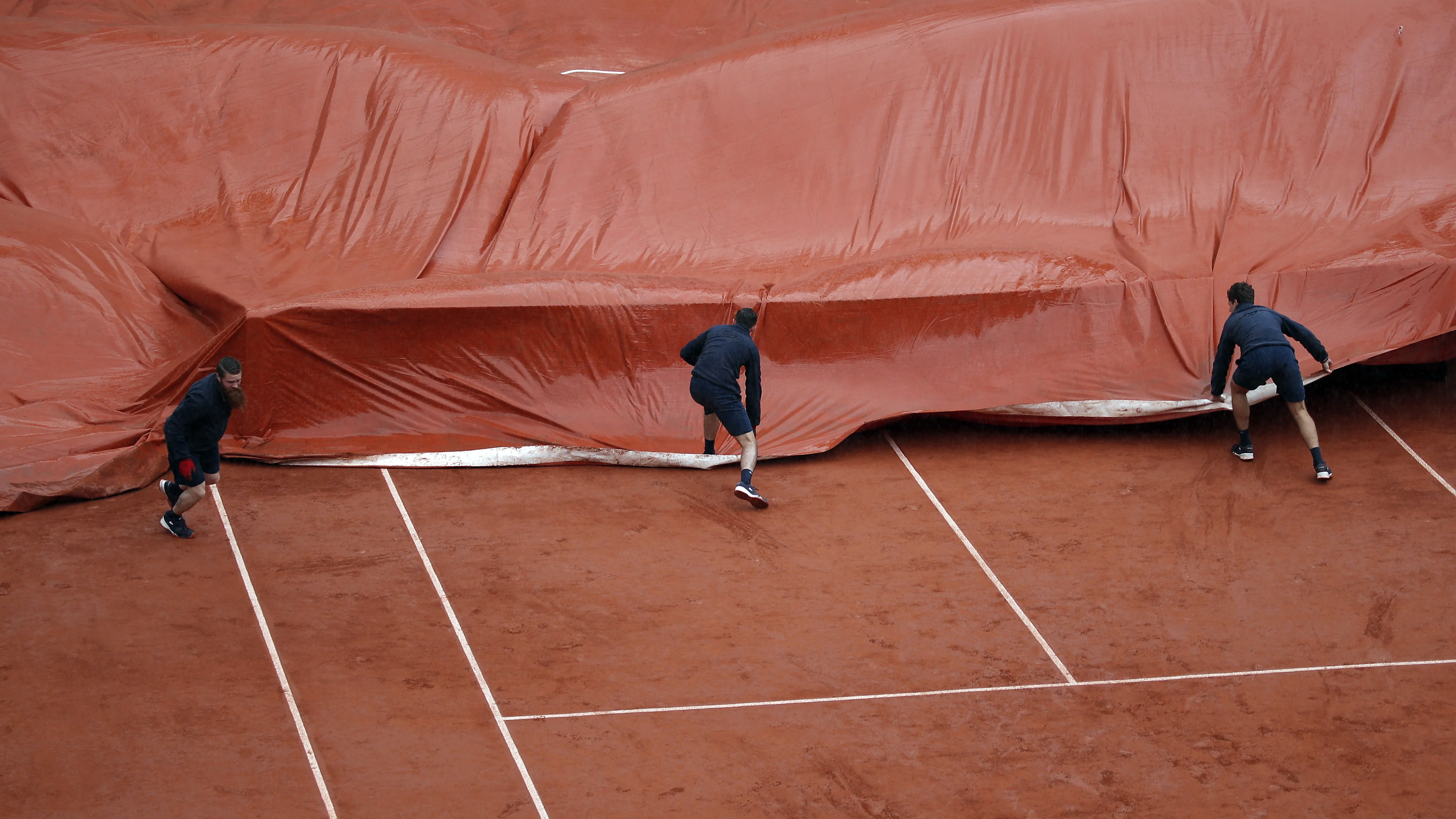 Los operarios de Roland Garros ponen la lona en la Philippe Chatrier