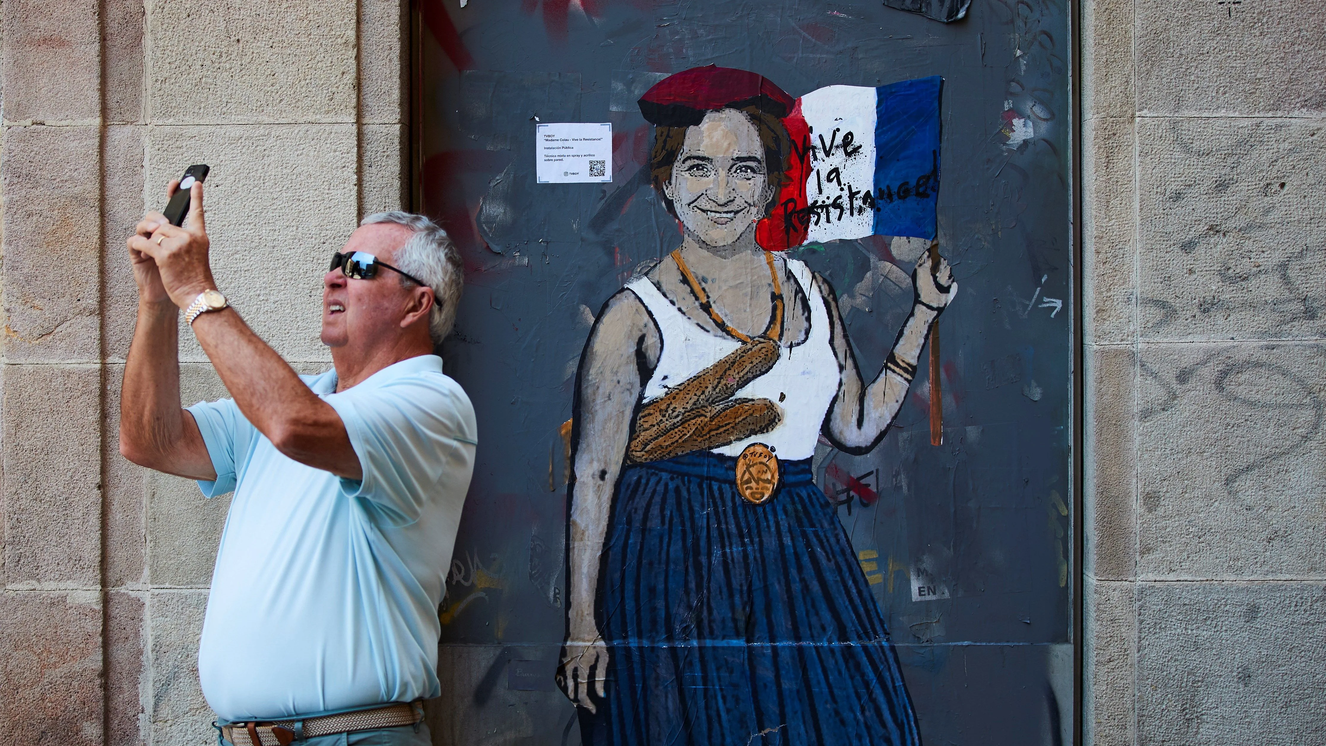 Un señor toma una fotografía junto al grafitti de 'madame Colau'