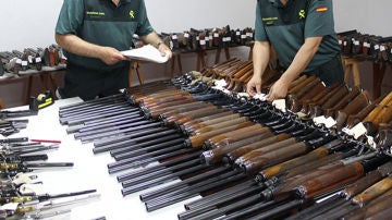 Dos agentes de la Guardia Civil revisan numerosas escopetas y armas