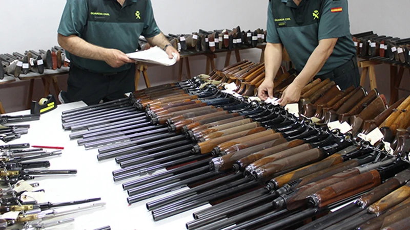 Dos agentes de la Guardia Civil revisan numerosas escopetas y armas