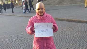 Delfina sostiene un cartel con el mensaje "vencí el cáncer"