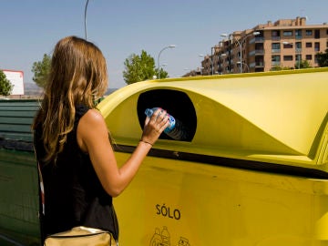 Una mujer deposita una botella de plástico en un contenedor amarillo. Una mujer deposita una botella de plástico en un contenedor amarillo.