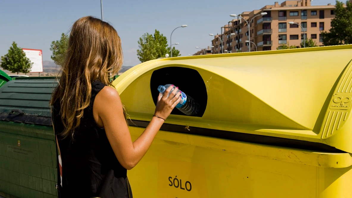 Una mujer deposita una botella de plástico en un contenedor amarillo.