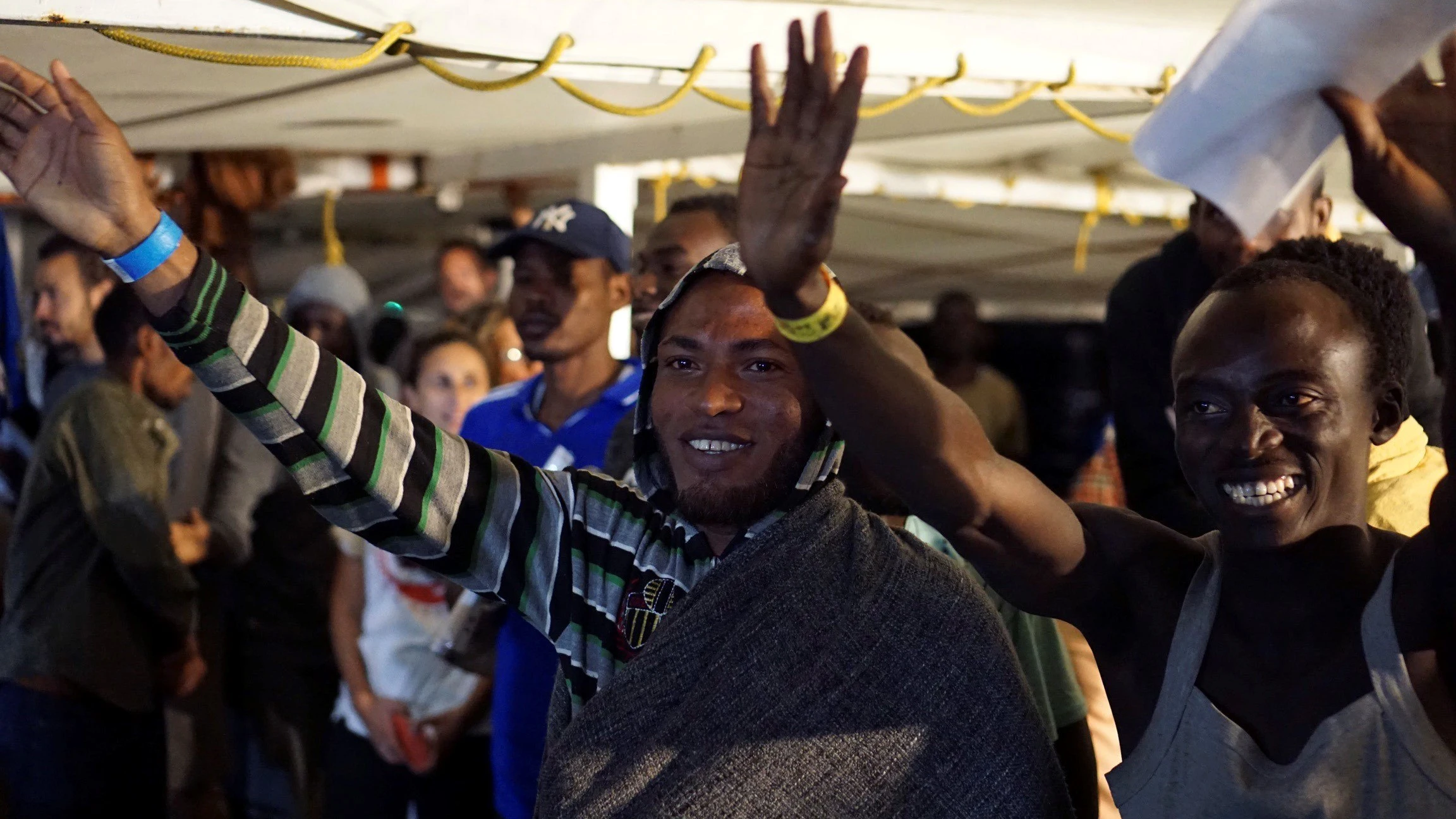 Algunos de los migrantes a bordo del Open Arms saludan momentos antes de desembarcar en Lampedusa