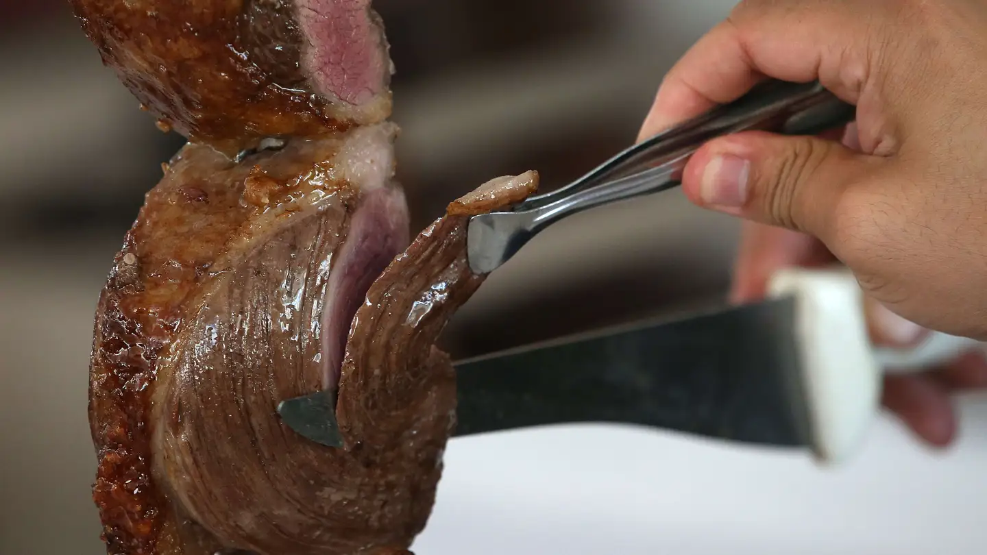Una persona corta carne en una churrasquería Una persona corta carne en una churrasquería