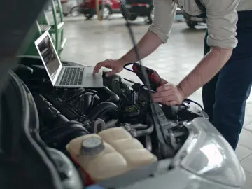 Un mecánico con el capó del coche abierto Un mecánico con el capó del coche abierto